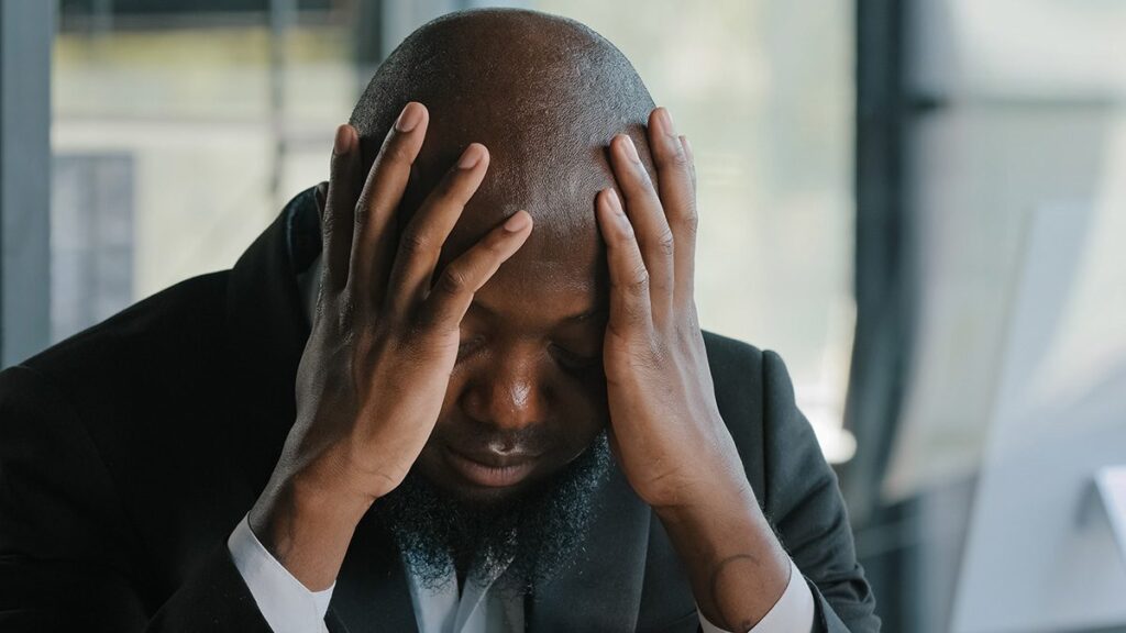 Sick exhausted black man suffering from headache syndrome and holding head in hands